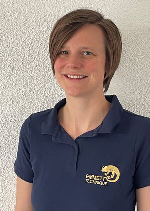Eine lächelnde Person in einem Polohemd mit dem Emmett Technique-Logo, vor einem weißen Hintergrund.