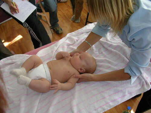 Eine Frau hält ein Baby, das auf einem Handtuch liegt. Eine andere Person macht Notizen.