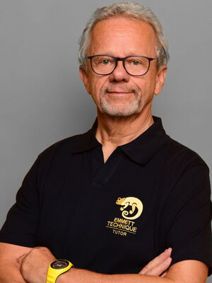 Ein Mann mit grauen Haaren und Bart, trägt eine Brille und ein schwarzes Poloshirt mit "Emmett Technique Tutor" Logo.