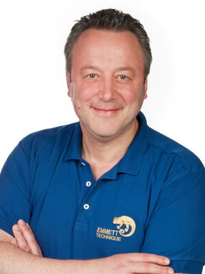 Es ist ein lächelnder Mann in einem blauen Hemd mit dem Emmett Technik-Logo.