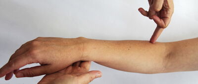 Eine Hand zeigt auf den Unterarm einer anderen Person.