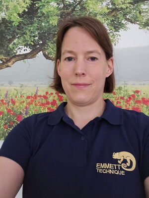 Eine Person im blauen Hemd mit "EMMETT TECHNIQUE" und einem Baum und Blumen im Hintergrund.