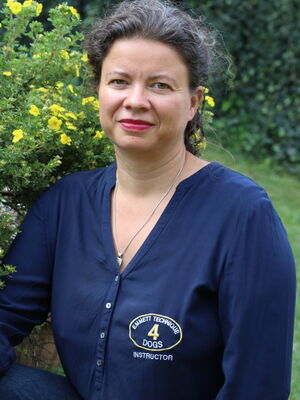 Eine Frau in blauer Bluse sitzt neben einem Strauch mit gelben Blumen im Garten.