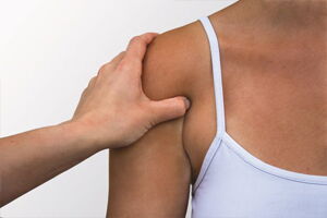 The image shows a person with a hand resting on their shoulder. The person is wearing a white tank top.