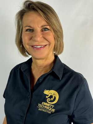 Eine lächelnde Frau in einem schwarzen Hemd mit "EMMETT TECHNIQUE INSTRUCTOR"-Logo.