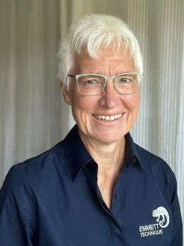 Es ist das Bild einer lächelnden Person mit weißem Haar und Brille.
