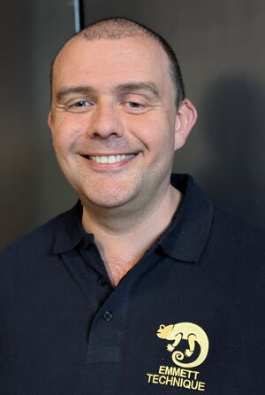 Ein lächelnder Mann in einem dunklen Polohemd mit "Emmett Technique" Logo.