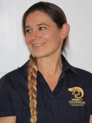 Es zeigt eine lächelnde Frau mit blondem Zopf. Sie trägt ein schwarzes Hemd mit „Emmett Technique Instructor“-Logo.